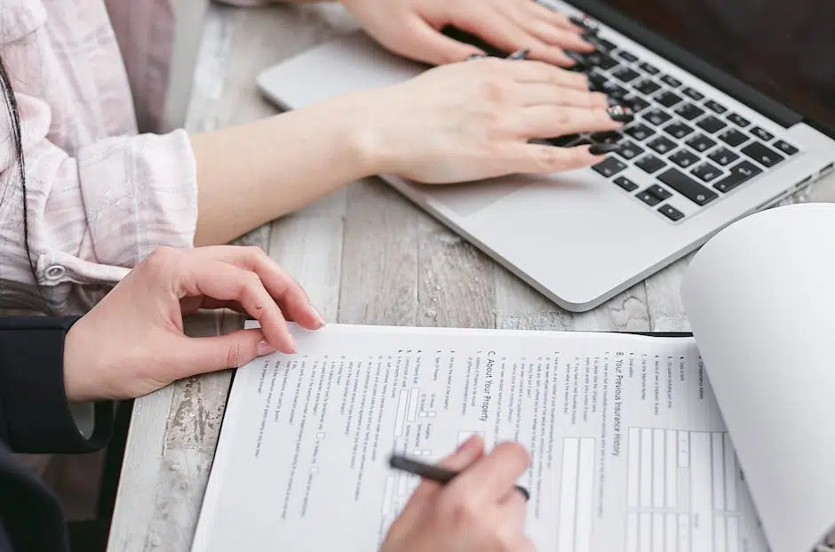 Hands typing on laptop and filling documents.