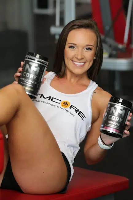 Person smiling, holding sports supplement containers in gym.