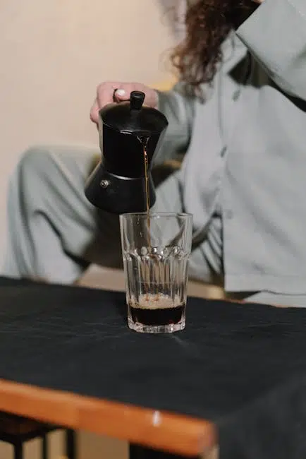 Person pouring coffee into glass on table.