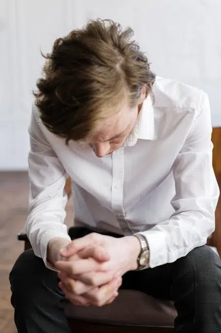 Person sitting, looking down with hands clasped.